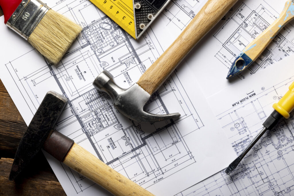 Narzędzia budowlane na planach technicznych mieszkania – młotek, śrubokręt, pędzel i poziomica przygotowane do odbioru technicznego lokalu.